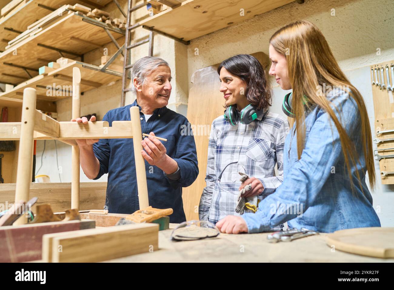 Un mentore esperto istruisce due giovani apprendisti sulle tecniche di lavorazione del legno in un vivace bosco. Il gruppo si impegna nell'apprendimento pratico e Foto Stock