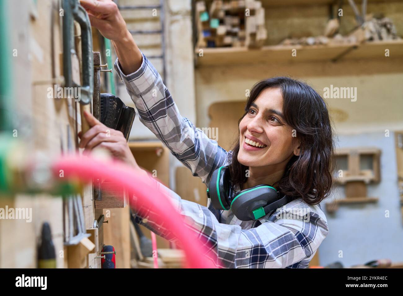 Una giovane donna che lavora entusiasticamente in un bosco, mostrando le sue abilità e la sua maestria artigianale. Indossando abiti a quadri e protettivi, si concentra su di lei Foto Stock