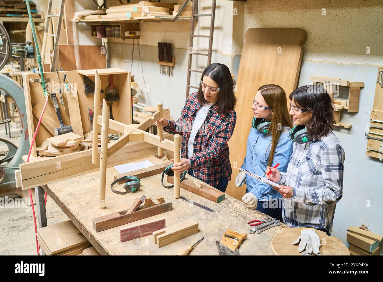 Un gruppo di giovani apprendisti impara le capacità di lavorazione del legno sotto la guida di un mentore esperto in un bosco. Il lavoro di squadra e la formazione pratica Foto Stock