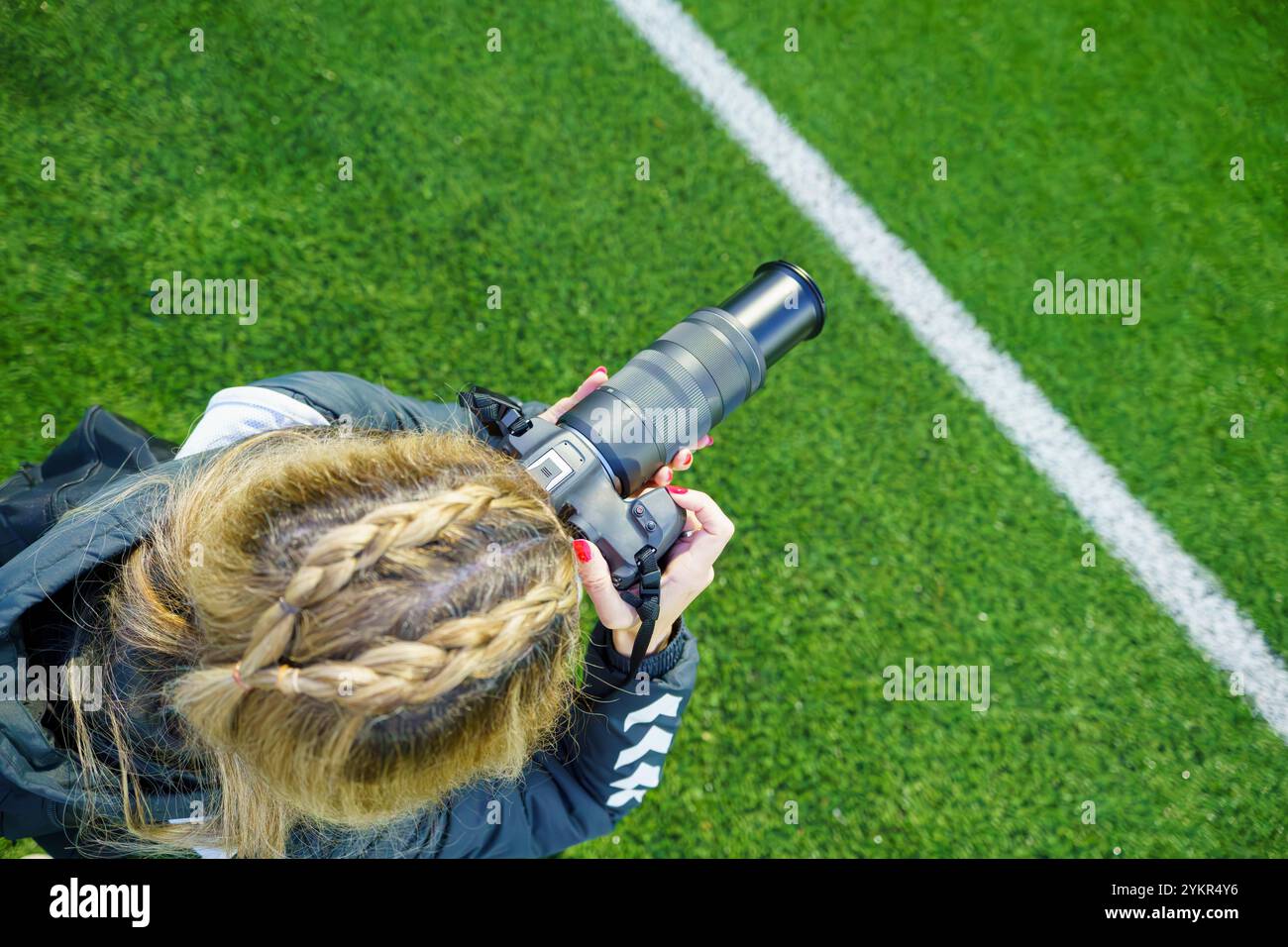 Vista dall'alto di una fotografa sportiva di mezza età che scatta foto su un campo di calcio durante una partita al crepuscolo Foto Stock