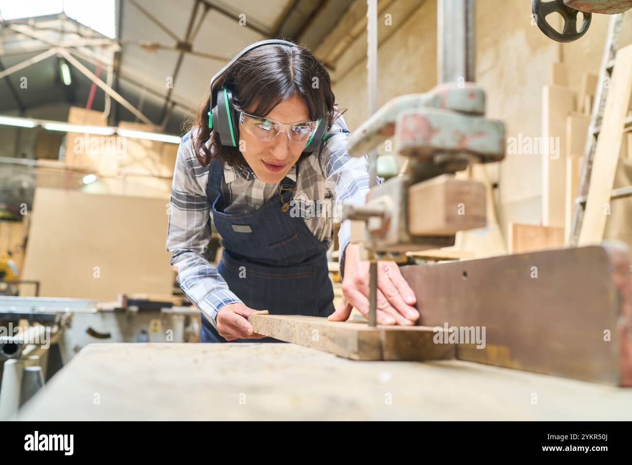 Una giovane donna che indossa gli indumenti di sicurezza gestisce le attrezzature in un fitto bosco. L'immagine cattura l'essenza dell'allenamento pratico e del lavoro di squadra in un bosco Foto Stock
