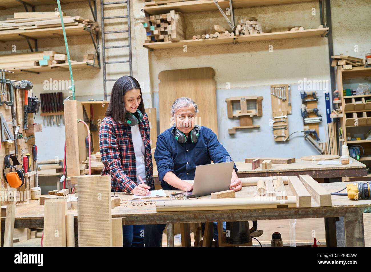 Un artigiano esperto guida un giovane apprendista in un bosco, sottolineando il lavoro di squadra e la capacità di costruire. La scena mostra la formazione pratica e. Foto Stock