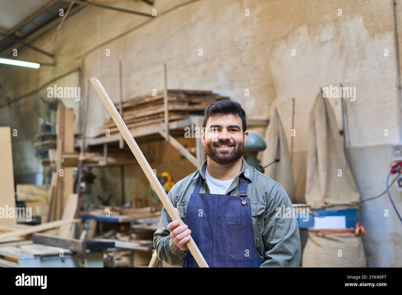 Ritratto di un lavoratore felice che tiene un pezzo di legno in un bosco. La scena raffigura un ambiente pratico e laborioso, sottolineando l'artigianalità Foto Stock