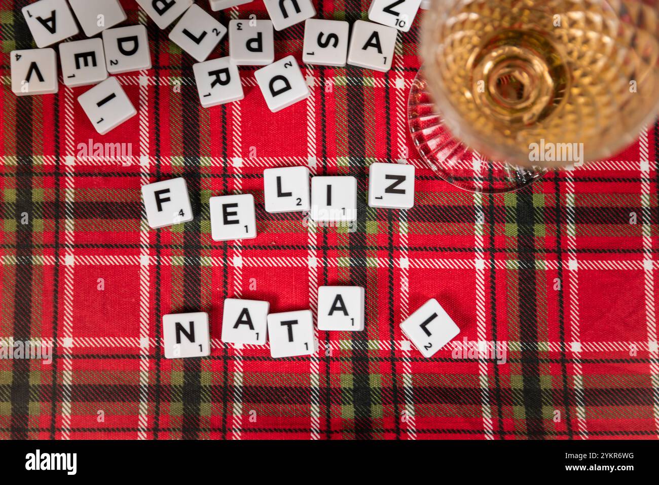 Vista dall'alto di una partita di Scrabble festosa su un tavolo a quadri rosso con un bicchiere di vino. "Feliz Natal", crea un'atmosfera natalizia accogliente. Foto Stock