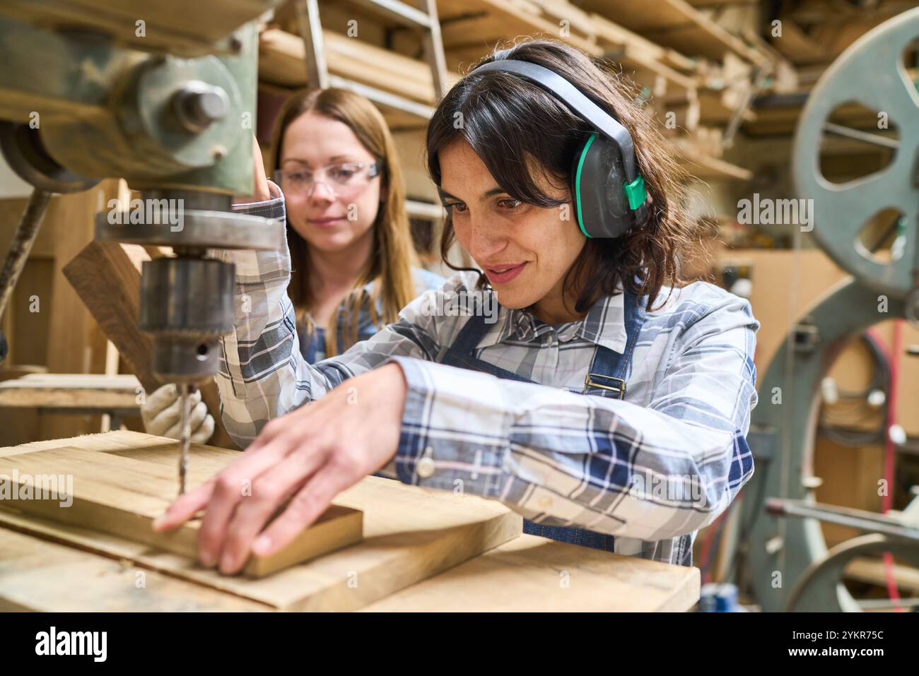 Due donne si impegnano in un progetto di lavorazione del legno in un bosco, sottolineando il lavoro di squadra e lo sviluppo di competenze pratiche. Un mentore più anziano guida un più giovane Foto Stock