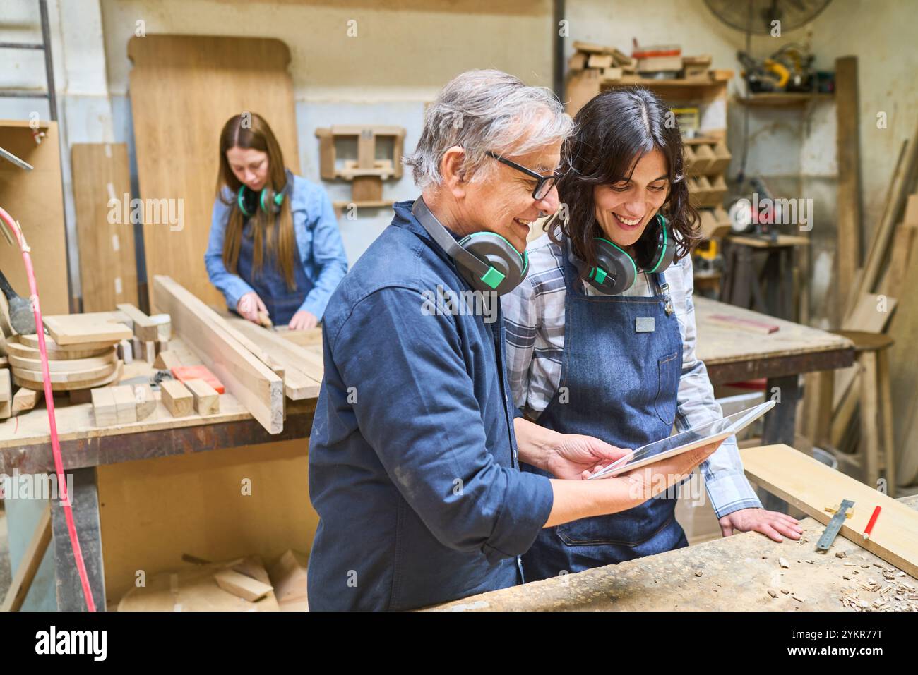 Un lavoratore più anziano e più giovane collabora in un bosco, mettendo in evidenza il lavoro di squadra e la formazione. Circondati da materiali in legno, si concentrano su un compito da svolgere Foto Stock