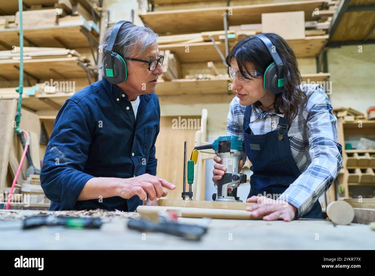 Un artigiano anziano fa da mentore a un giovane apprendista in un bosco, sottolineando il lavoro di squadra e lo sviluppo delle competenze. Sono impegnati in lavori con attrezzi e WO Foto Stock