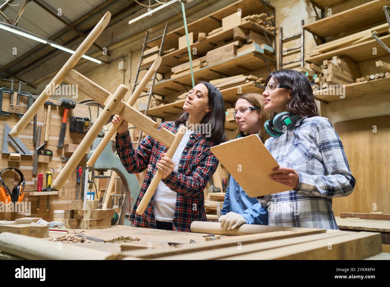 Un gruppo eterogeneo di persone che lavorano insieme in un bosco. La scena enfatizza il lavoro di squadra, la formazione e il tutoraggio in un ambiente di lavorazione del legno. Foto Stock