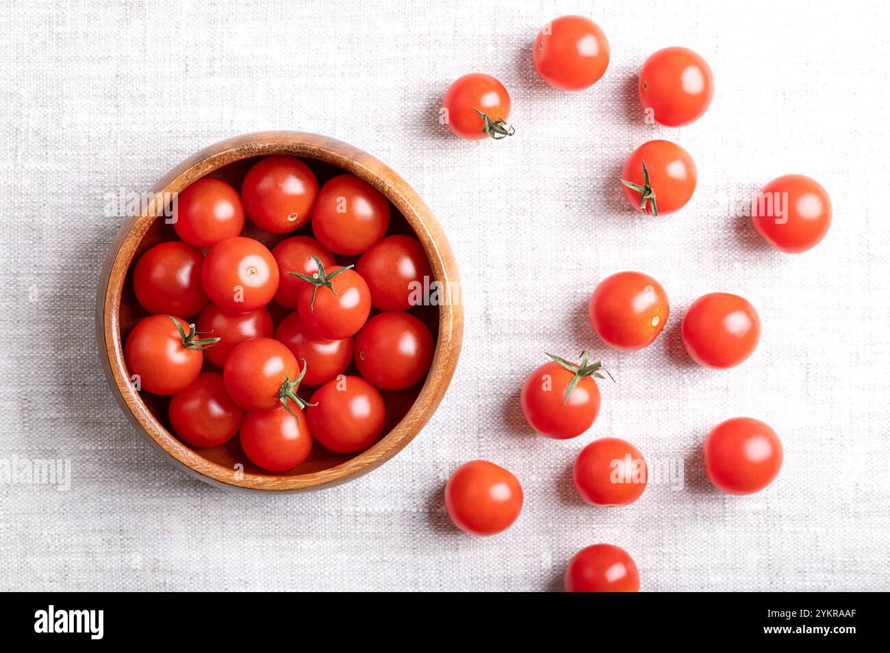 Pomodori ciliegini rossi piccoli in una ciotola di legno su tessuto di lino, dall'alto. Pomodori da cocktail freschi, maturi, piccoli e rotondi. Foto Stock