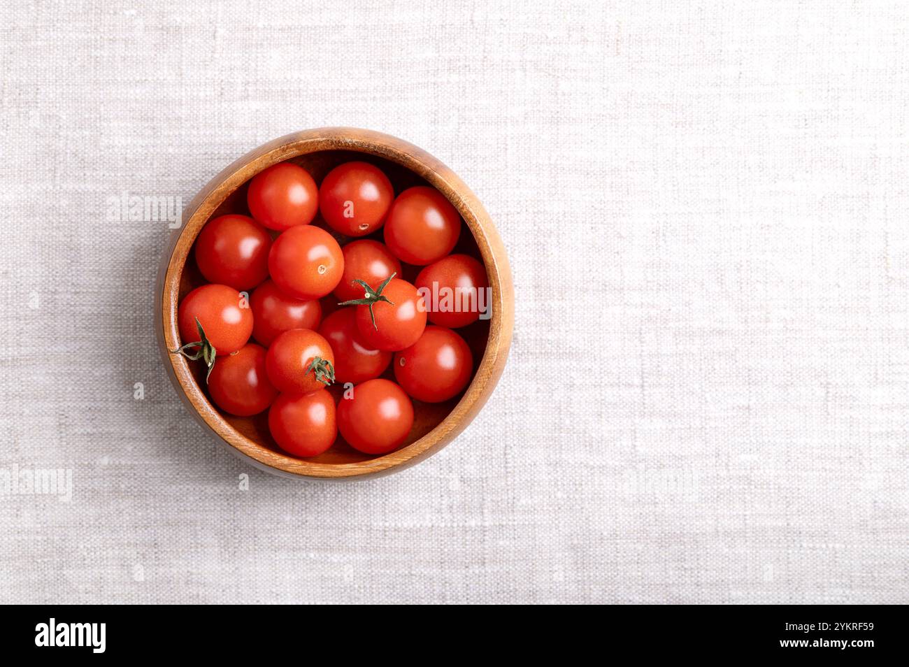 Pomodori ciliegini rossi piccoli in una ciotola di legno su tessuto di lino, dall'alto, con spazio vuoto per il testo. Pomodori da cocktail freschi, maturi, piccoli e rotondi. Foto Stock