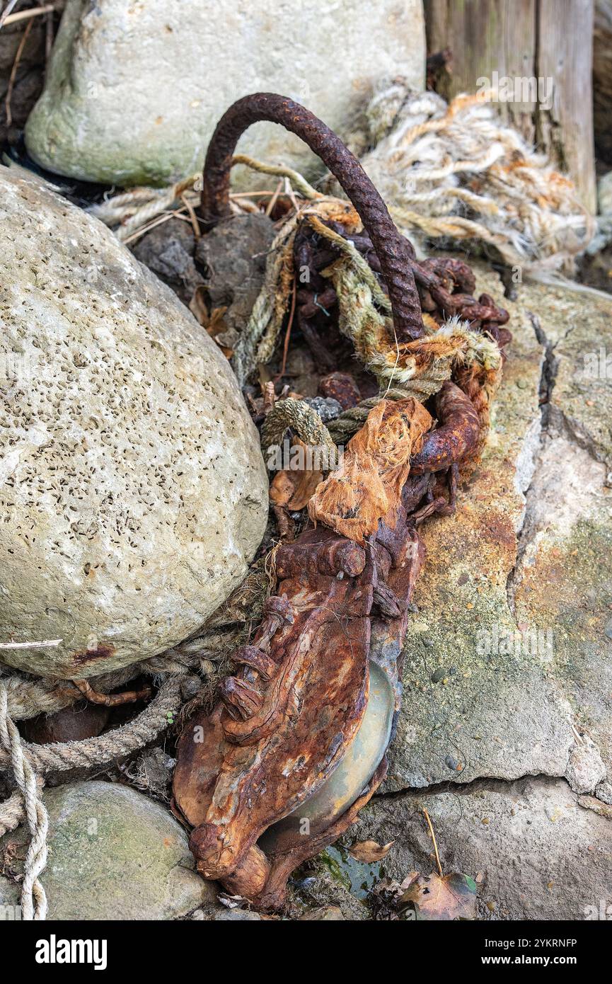 vecchio blocco arrugginito e paranco a sinistra per marcire tra le rocce sulla riva del mare. Foto Stock