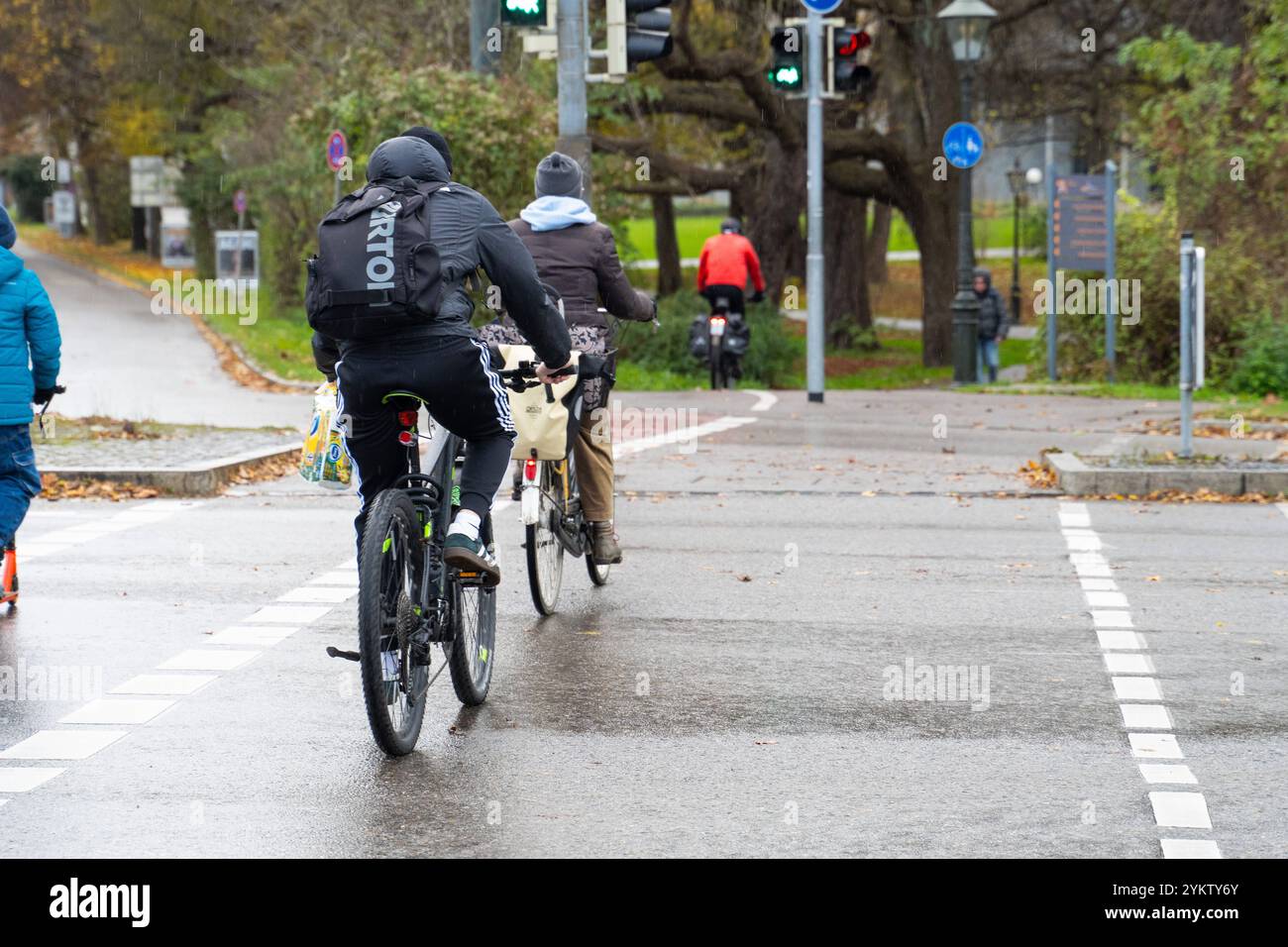 Augusta, Baviera, Germania - 18 novembre 2024: Ciclista al semaforo in autunno. Simbolo per andare in bicicletta sotto la pioggia o su una strada bagnata nel traffico. *** Radfahrer fahren im Herbst-Wetter an einer Verkehrsampel. Symbol für Fahrrad fahren bei Regen, bzw. nasser Fahrbahn im Straßenverkehr. Foto Stock