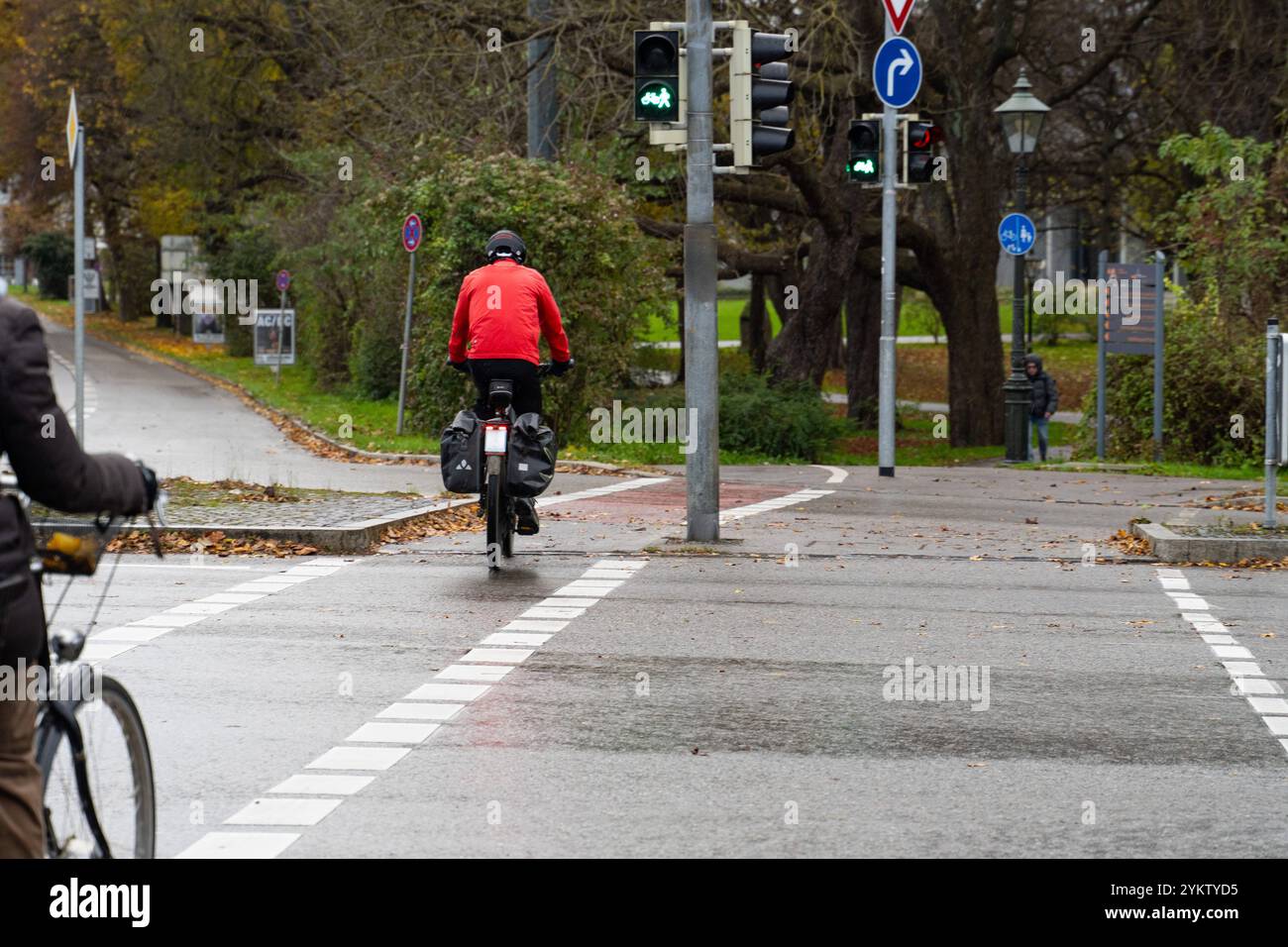 Augusta, Baviera, Germania - 18 novembre 2024: Ciclista al semaforo in autunno. Simbolo per andare in bicicletta sotto la pioggia o su una strada bagnata nel traffico. *** Radfahrer fahren im Herbst-Wetter an einer Verkehrsampel. Symbol für Fahrrad fahren bei Regen, bzw. nasser Fahrbahn im Straßenverkehr. Foto Stock