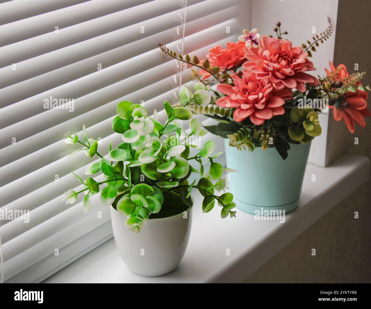 Piante artificiali luminose in vasi sul davanzale, fiori rossi sulla finestra Foto Stock