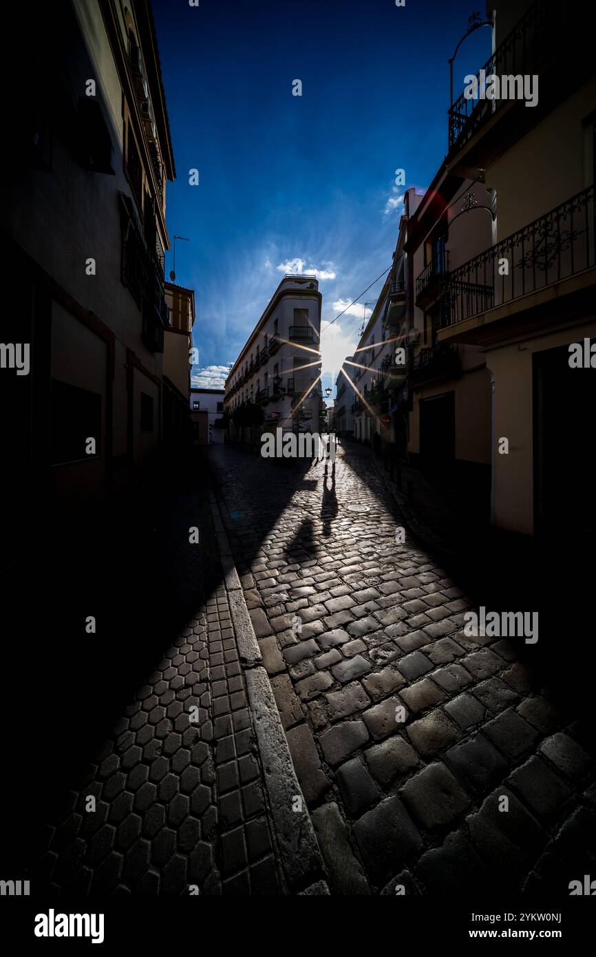 Un bellissimo tramonto getta ombre spettacolari nel centro storico di Siviglia, in Spagna. Il sole illumina dolcemente la strada acciottolata di Calle Feria, Foto Stock