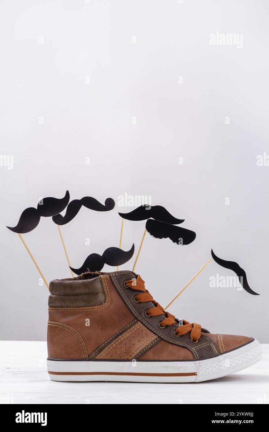 Scatto verticale di sneaker marrone con baffi cartoni animati. Scarpa da uomo con spazio copia su bianco Foto Stock