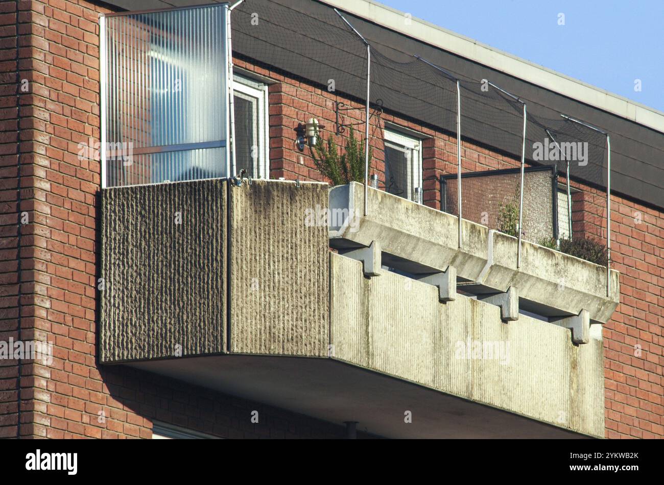 Vista ravvicinata di un balcone in cemento con recinzione in plexiglas e rete per uccelli, attaccato ad un edificio in mattoni Foto Stock