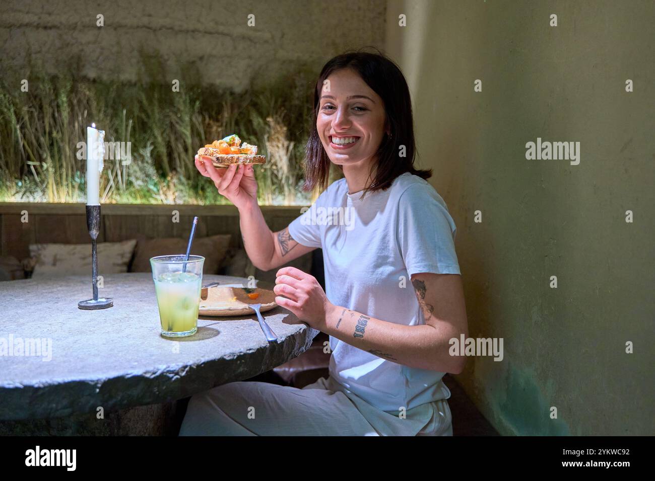 Una donna è seduta a un tavolo con un piatto di cibo e un drink. Sta sorridendo e si sta godendo il suo pasto Foto Stock