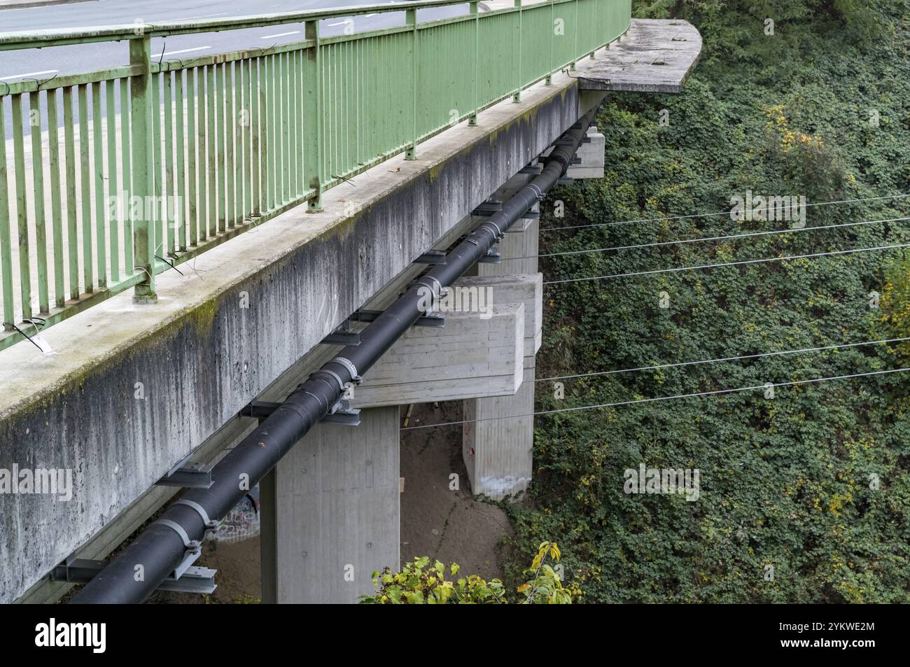 I tubi neri spessi sono fissati sotto un ponte di cemento con una ringhiera in metallo verde Foto Stock