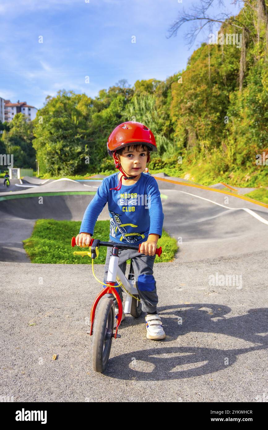 Un ragazzo che indossa un casco corre in bicicletta lungo una strada. Il ragazzo indossa una camicia blu e pantaloni grigi Foto Stock