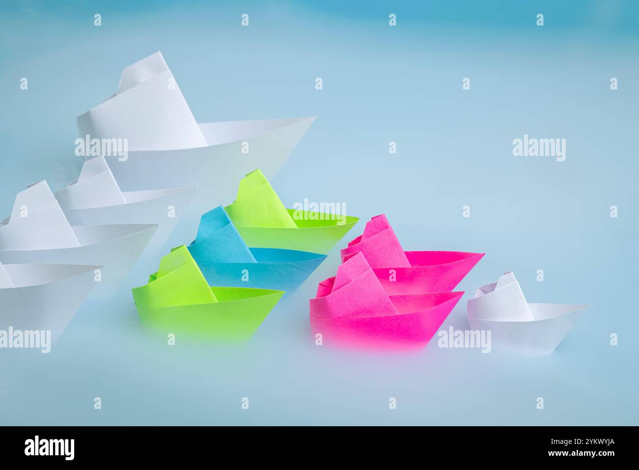 Una piccola barca di carta bianca che conduce altre barche colorate su uno sfondo blu nebbioso che simboleggia il mare. Concetto di leadership. Foto Stock