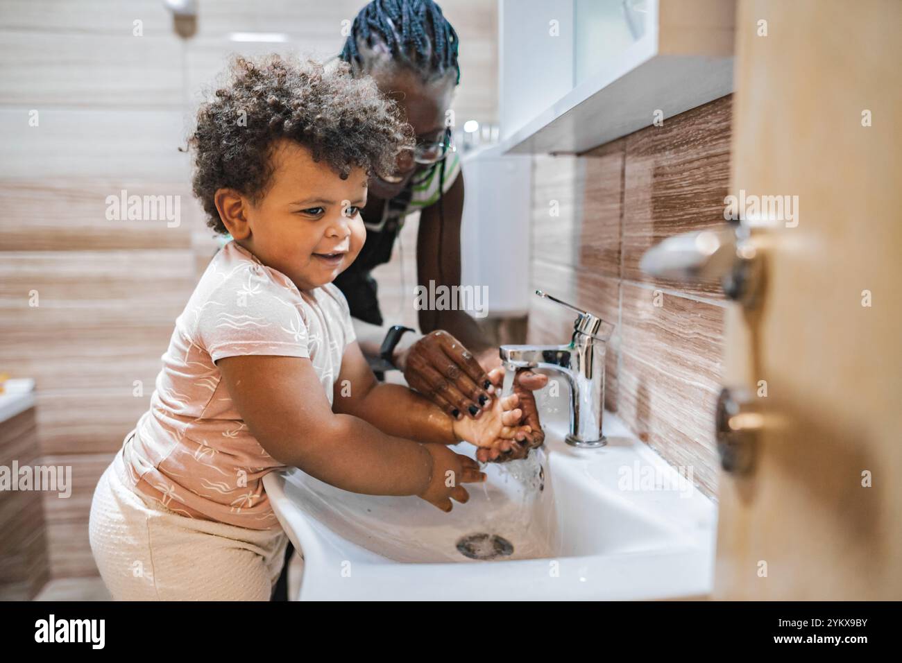 Un bambino allegro impara a lavarsi le mani in un accogliente ambiente del bagno Foto Stock