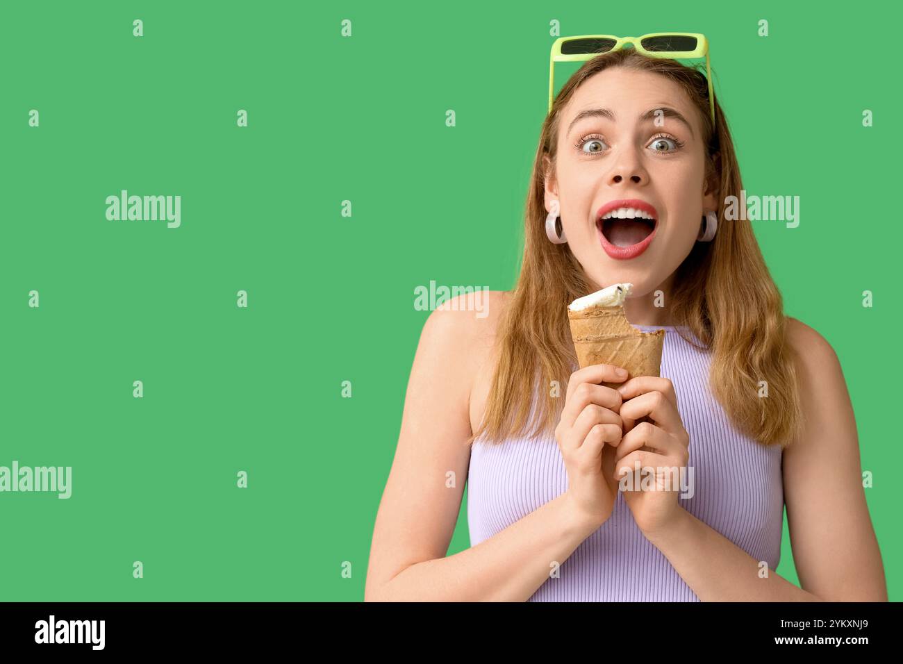 Una giovane donna ha sorpreso con un gelato alla vaniglia morso in una tazza di cialde su sfondo verde Foto Stock