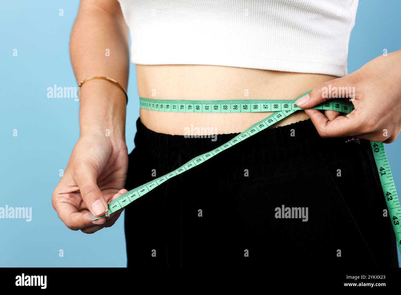 Slim Asian Young Woman che misura la sua vita usando il nastro di misurazione, isolato su sfondo blu Foto Stock