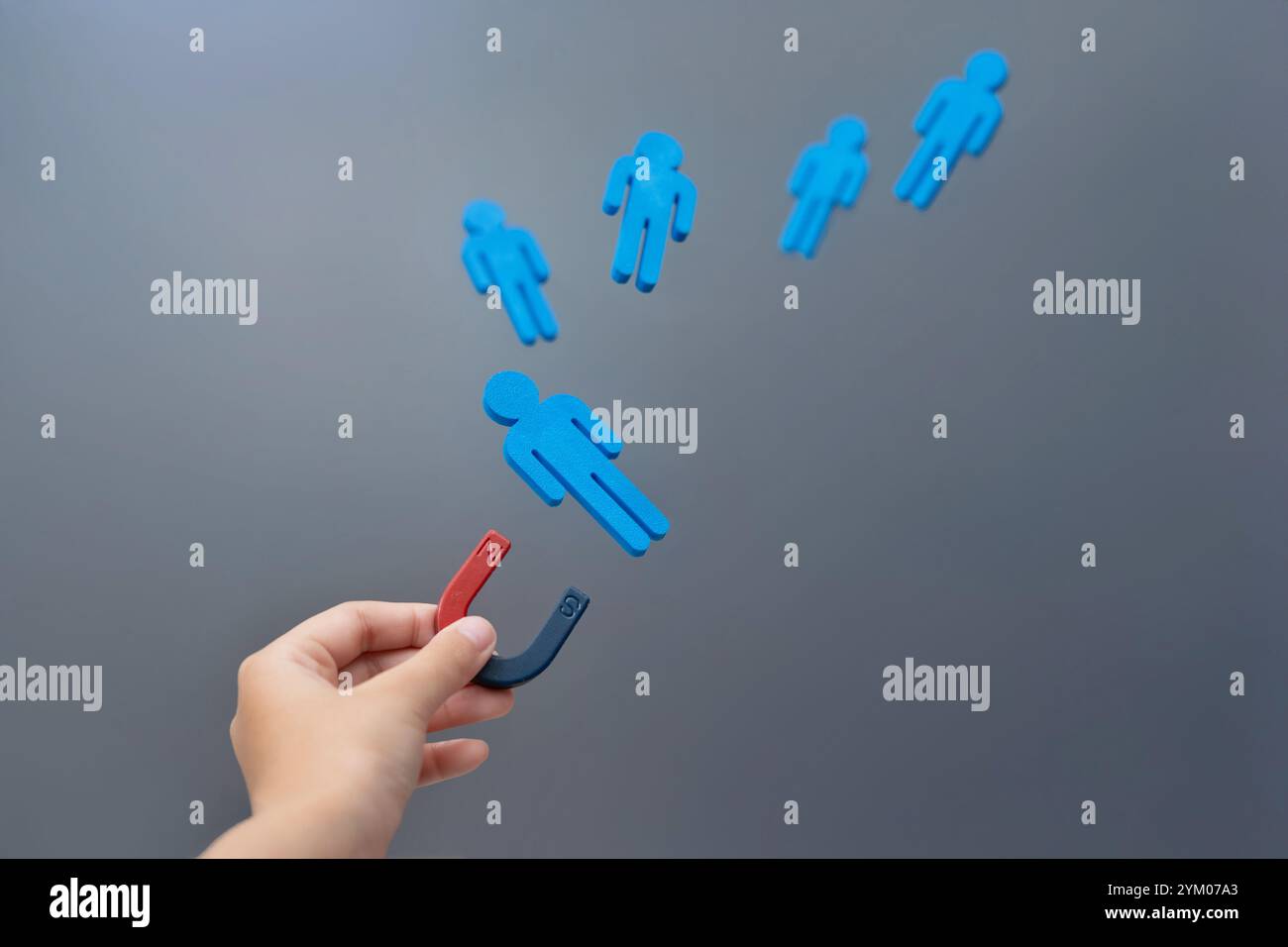 Una mano che tiene in mano un magnete attira figure di legno blu. Concetto di attrazione. Foto Stock