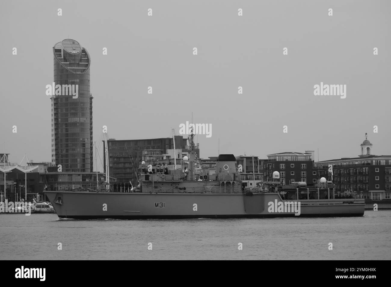 Scala di grigi, passando per l'edificio del rossetto. La HMS Cattistock, una dragamine della Royal Navy Hunt Class, ritorna alla sua base di casa, Portsmouth, dopo essere stata coinvolta in una settimana di operazioni per monitorare due gruppi di lavoro della Marina russa che passano il Regno Unito, lavorando fianco a fianco con le altre navi, la RAF e gli alleati della NATO. Foto Stock