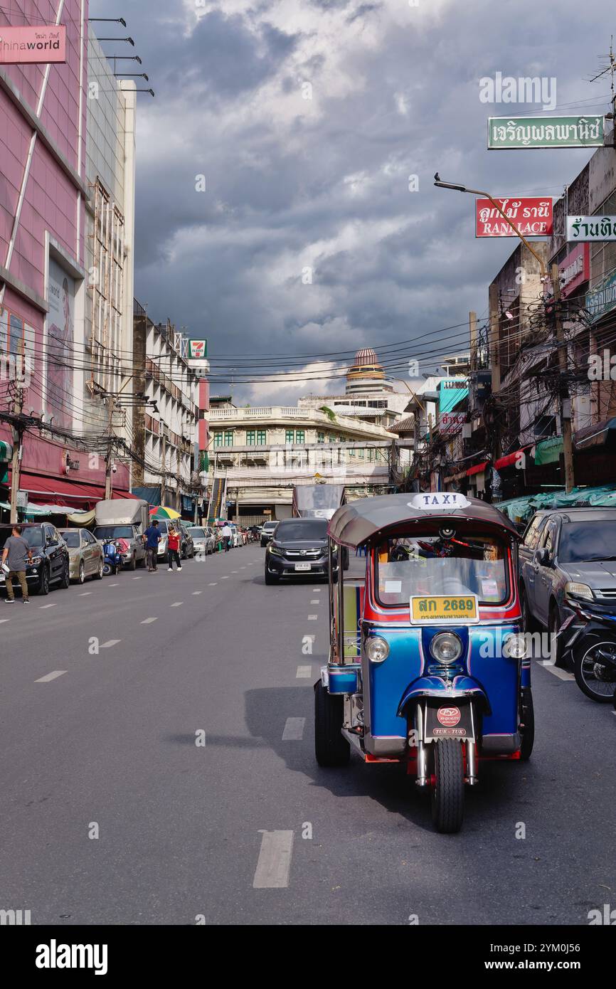 Un tipico tuk-tuk tailandese, un taxi a tre ruote, in una strada a Pahurat, Bangkok, Thailandia, con nuvole di pioggia scure che si incombono sopra la testa Foto Stock