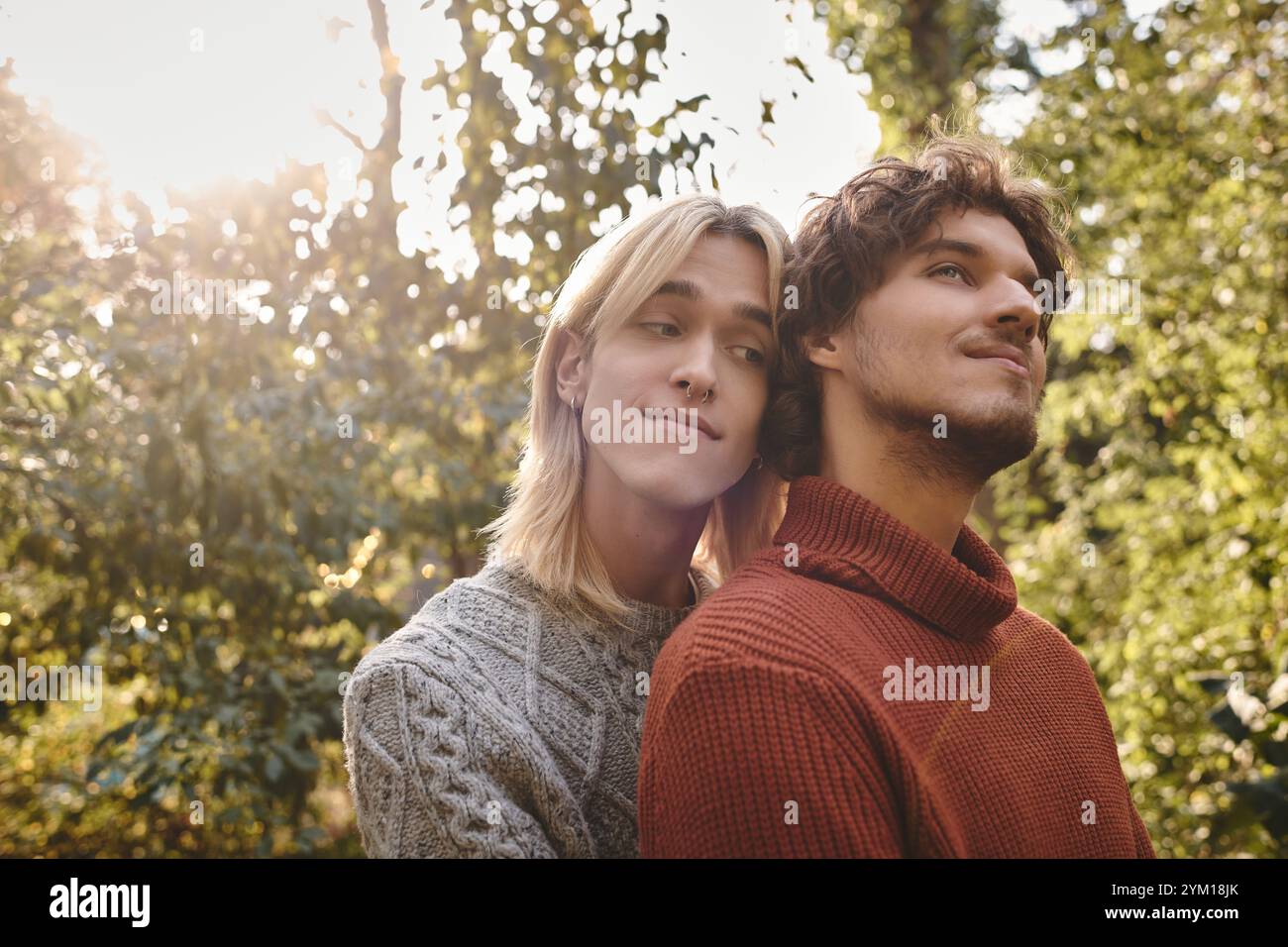 In una tranquilla foresta durante l'ora d'oro, due giovani uomini si abbracciano calorosamente circondati dalla natura. I loro sorrisi riflettono gioia e intimità, mostrando un beauti Foto Stock