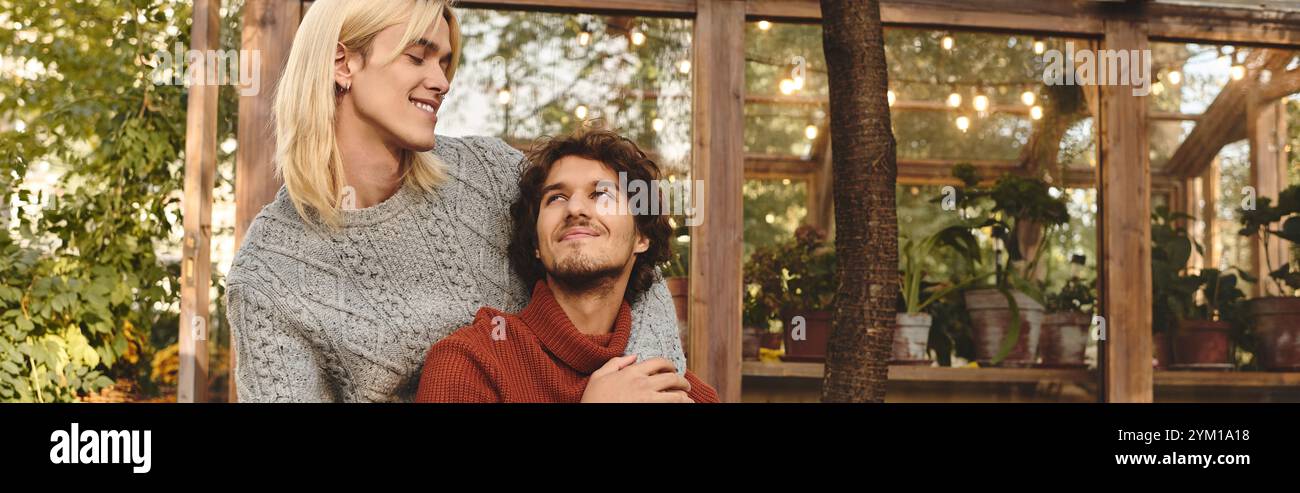 Due giovani uomini condividono un momento affettuoso in un caffè in giardino, circondato da vegetazione lussureggiante e luci scintillanti. I loro sorrisi e il loro calore creano un invit Foto Stock