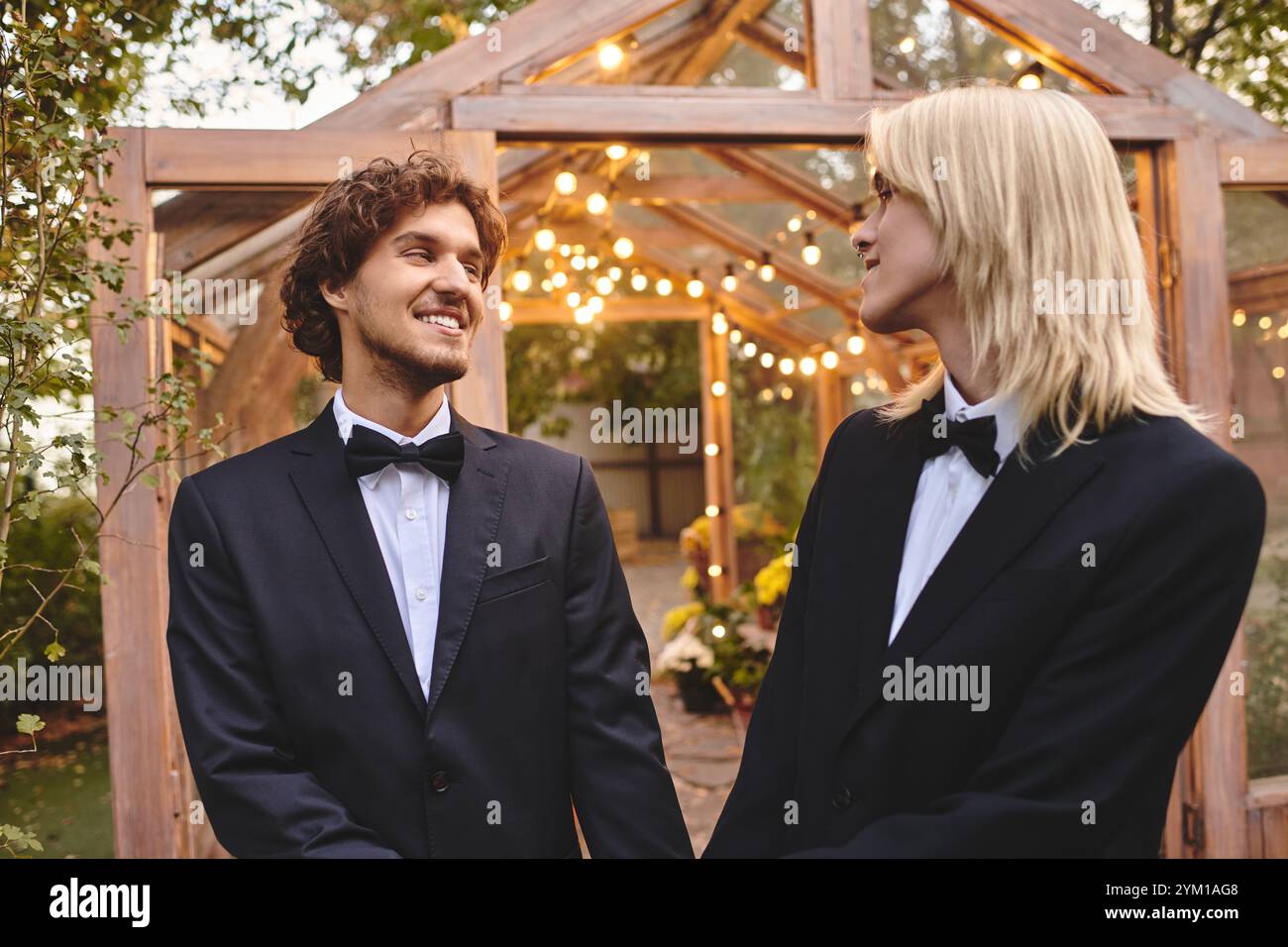 Due giovani in abbigliamento formale condividono un momento di gioia in un ambiente all'aperto splendidamente illuminato. L'incantevole giardino è adornato da luci scintillanti, cre Foto Stock
