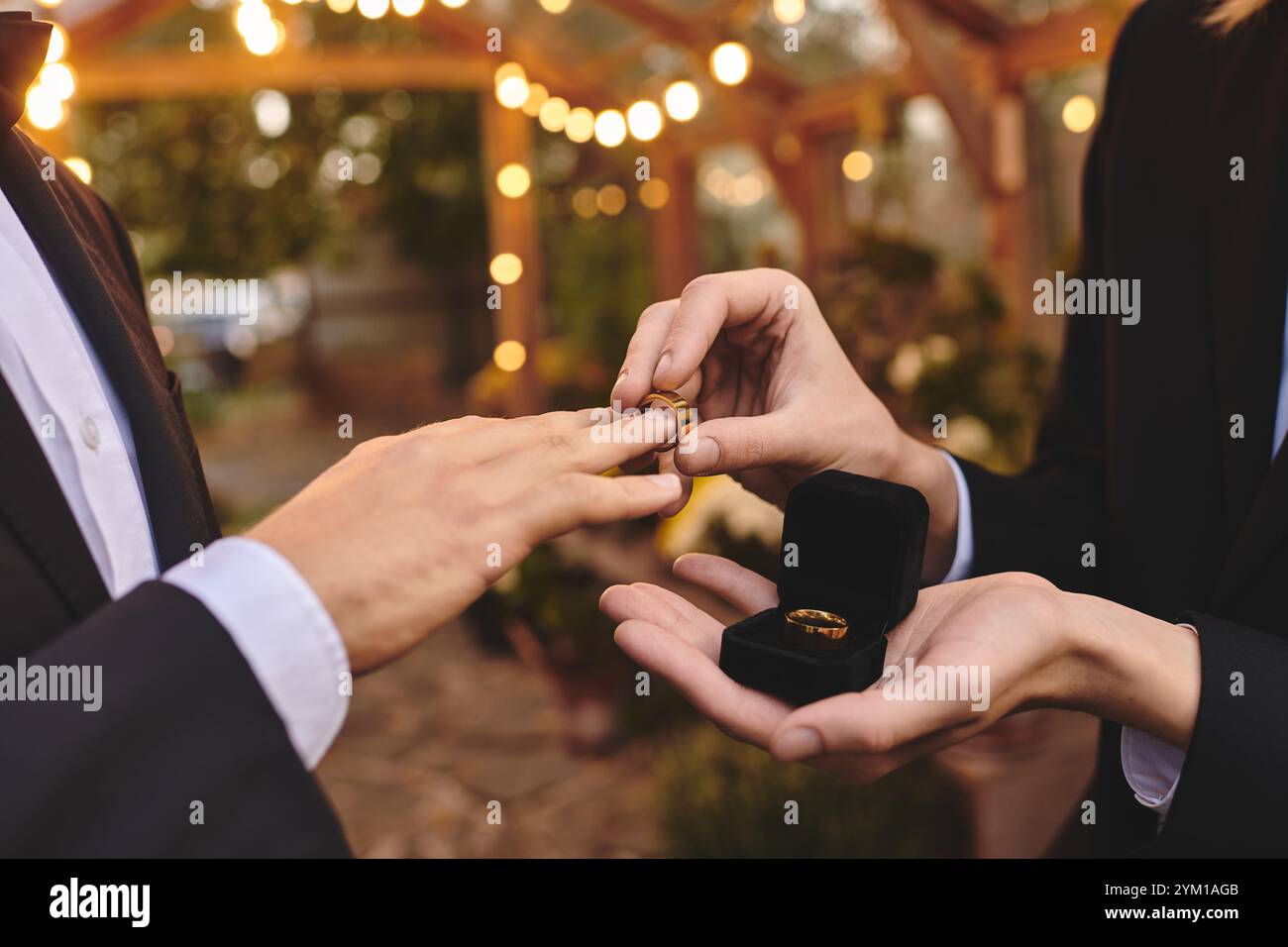 In un romantico giardino adornato da luci scintillanti, due giovani si scambiano le fedi nuziali, abbracciando il loro amore. Il momento cattura gioia, impegno, a. Foto Stock