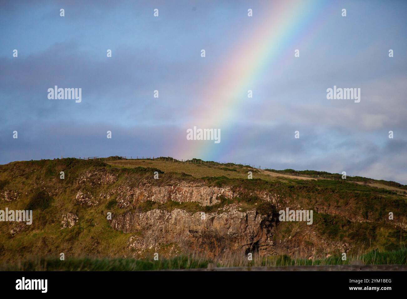 Arcobaleno sopra una scogliera erbosa in Irlanda con cieli blu e nuvole drammatiche Foto Stock