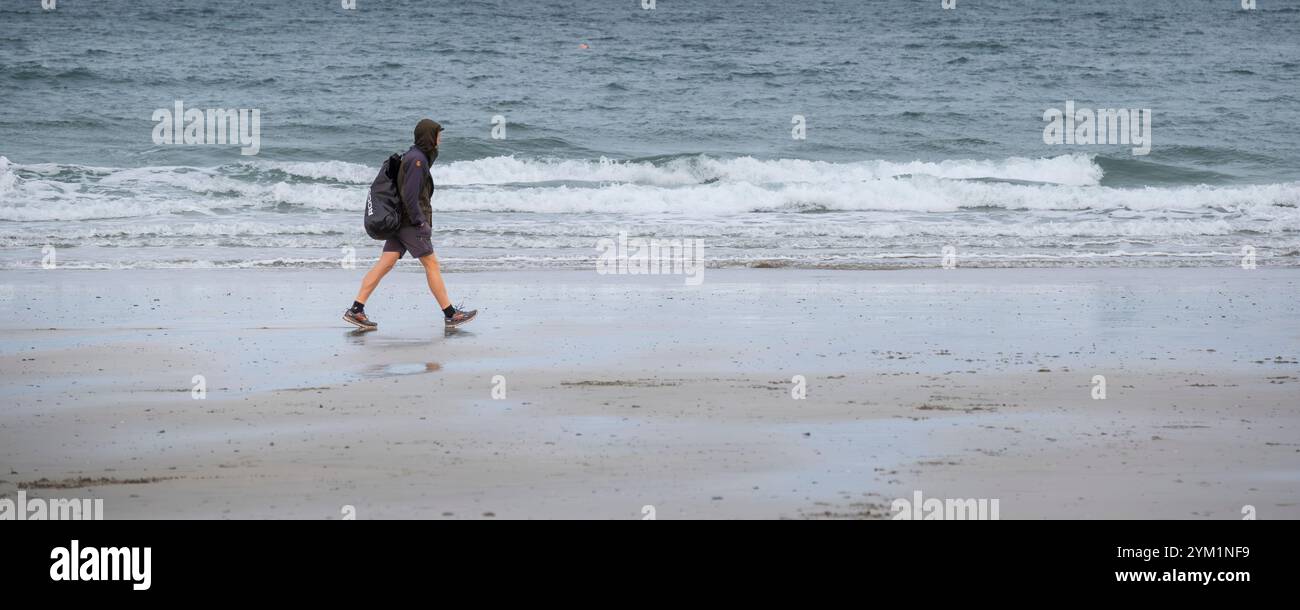 Un'immagine panoramica di un camminatore con uno zaino che cammina da solo lungo la costa di Towan Beach a Newquay in Cornovaglia nel Regno Unito Foto Stock