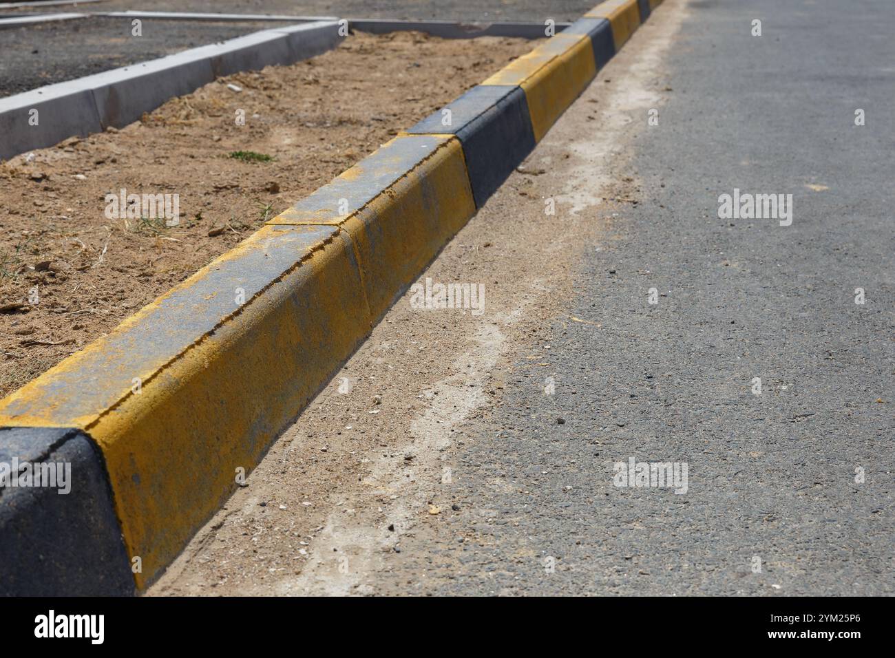 Un cordolo a righe giallo e nero. bordo marciapiede e strada asfaltata Foto Stock