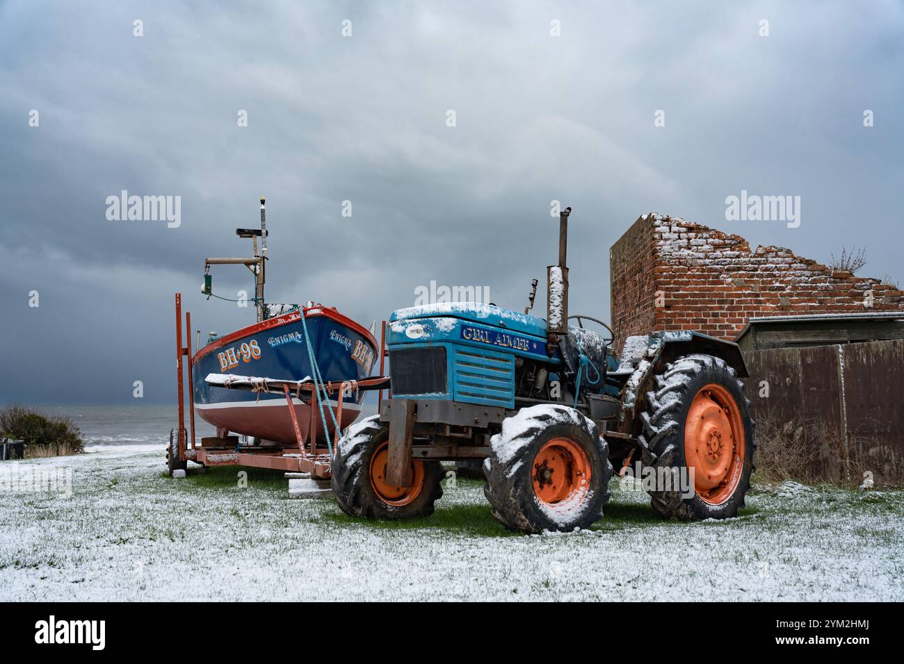 Un trattore blu e una piccola barca da pesca presso il campo di barche Cullercoats sulla neve Foto Stock