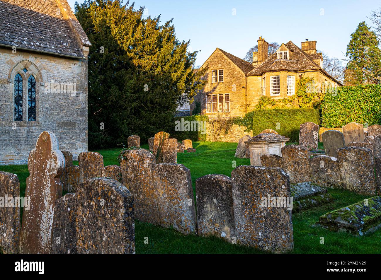 Luce serale sull'Old Rectory vista dal cimitero della chiesa di San Giovanni Battista nel villaggio Cotswold di Great Rissington, Gloucestershire Foto Stock