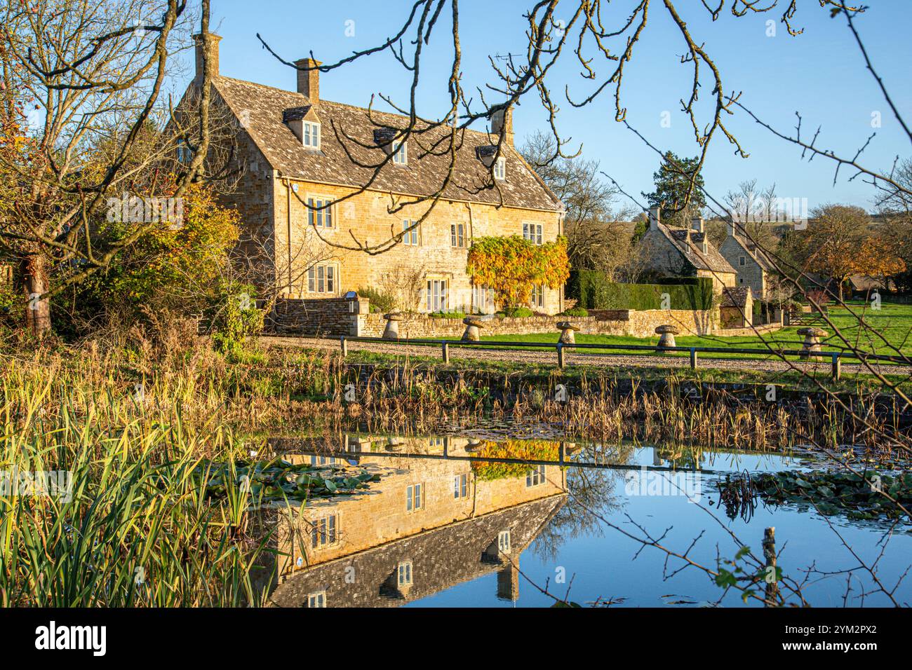 Luce serale sulla College Farm accanto allo stagno sul verde nel villaggio Cotswold di Wyck Rissington, Gloucestershire, Inghilterra Regno Unito Foto Stock
