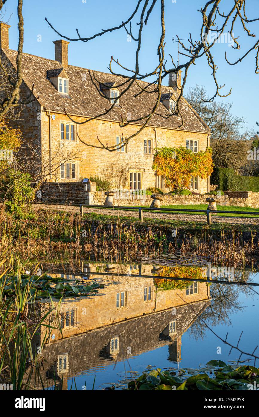 Luce serale sulla College Farm accanto allo stagno sul verde nel villaggio Cotswold di Wyck Rissington, Gloucestershire, Inghilterra Regno Unito Foto Stock