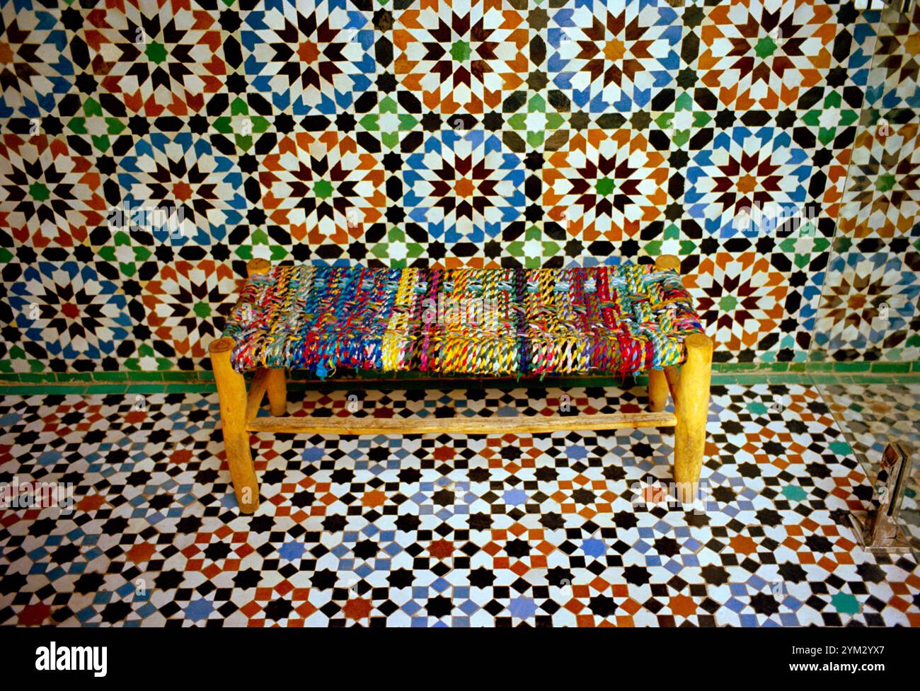 Una panchina contro le piastrelle geometriche nella tranquilla Madrassa di Ben Youssef o scuola nel suk di Marrakech in Marocco nel Maghreb in Nord Africa Foto Stock