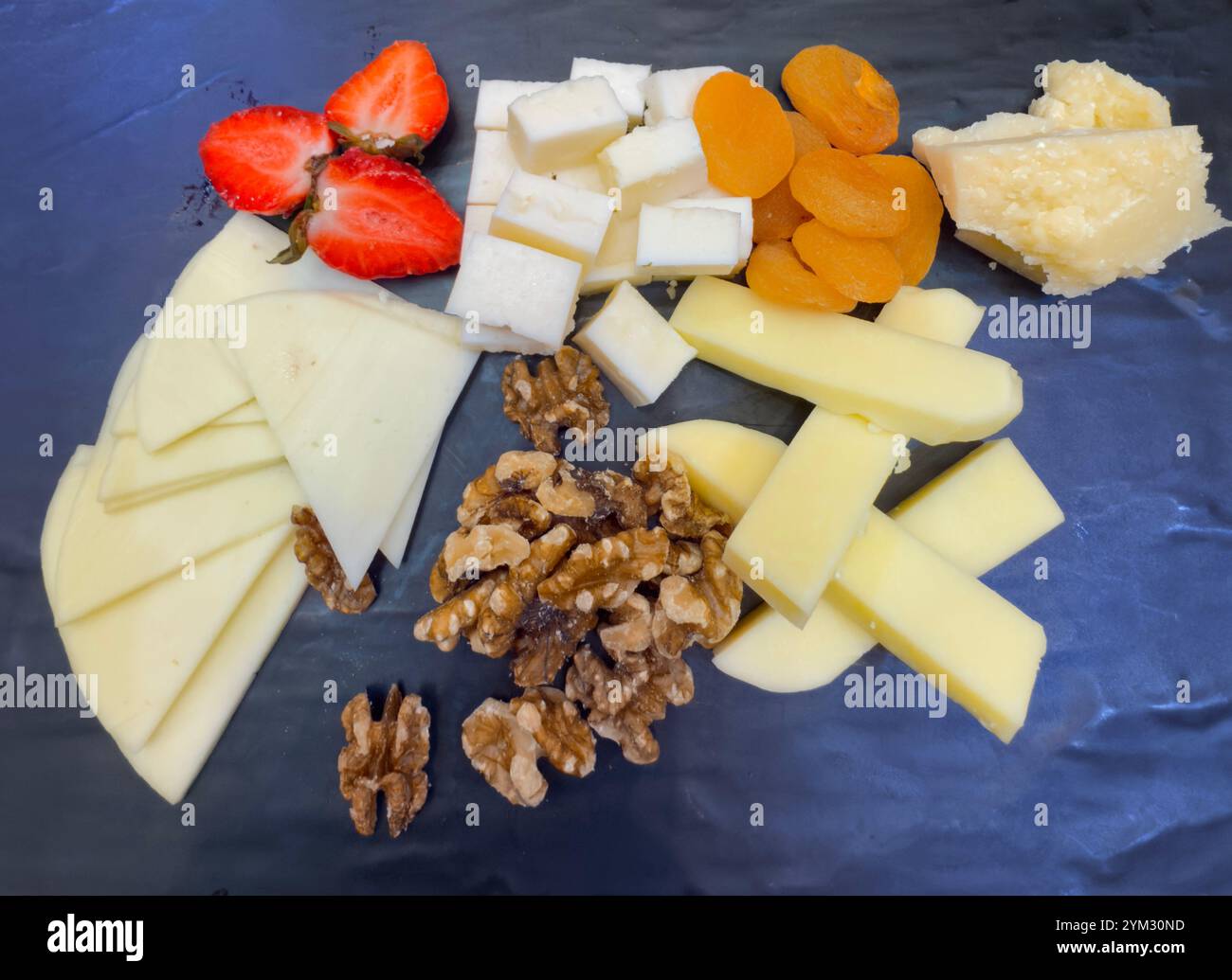 Selezione di formaggi su tavola di ardesia nera con albicocche, noci e fragole a metà Foto Stock