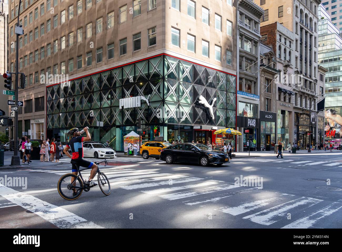 Un uomo con biciclette in attesa al semaforo con il negozio PUMA Flagship sulla 5th Avenue sullo sfondo. Foto Stock