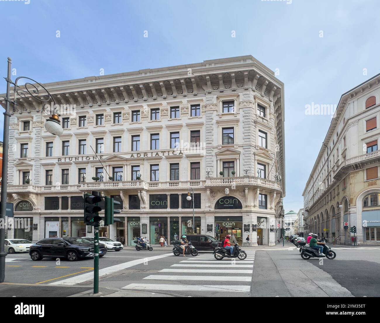 Trieste, Italia - 27 giugno 2024: Riunione Adriatica edificio storico con negozio di lusso Coin a livello strada, paesaggio stradale con auto, moto Foto Stock