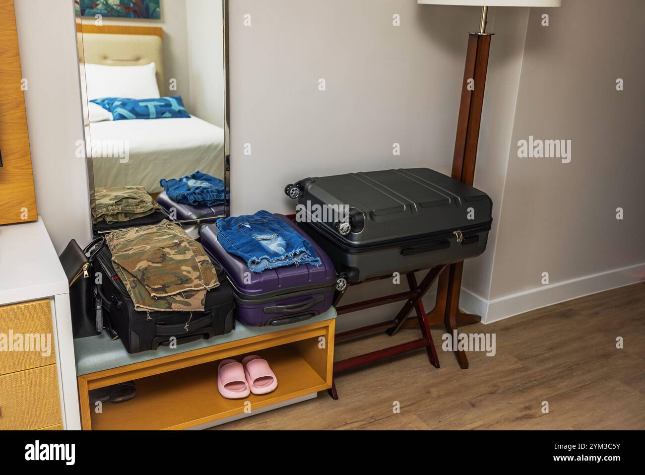 Valigie imballate con abiti piegati all'interno della camera dell'hotel con specchio, pavimento in legno e pantofole rosa sullo scaffale. Miami Beach. STATI UNITI. Foto Stock