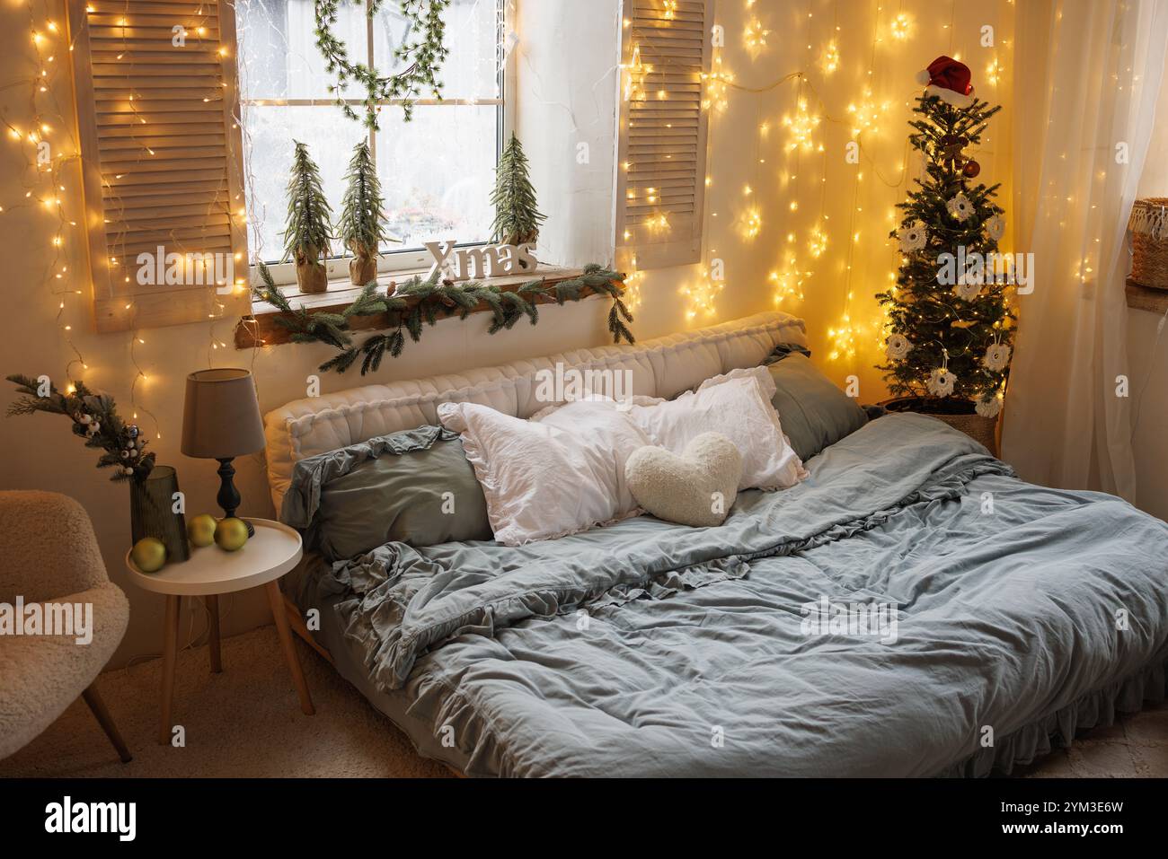 Accogliente camera da letto invernale scandinava con luci natalizie, arredi e albero di Natale in un'atmosfera calda Foto Stock