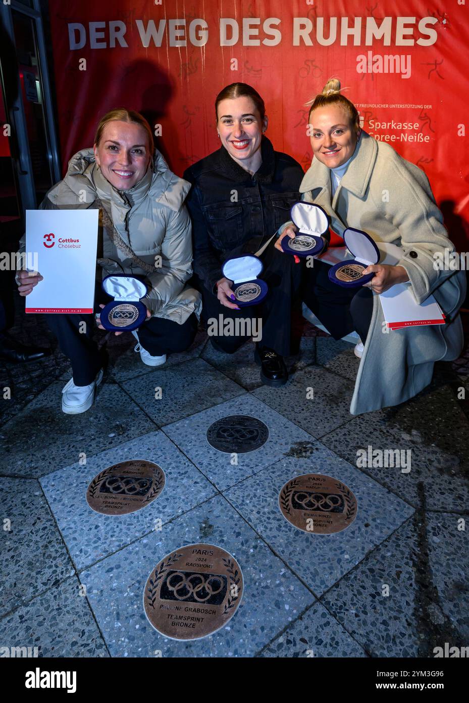 20 novembre 2024, Brandeburgo, Cottbus: I ciclisti Emma Hinze (l-r), Pauline Grabosch e Lea Sophie Friedrich siedono di fronte al municipio di Cottbus mentre ricevono le loro nuove targhe per "la strada della gloria". Gli atleti hanno vinto tutte le medaglie ai Giochi Olimpici di Parigi del 2024. Queste targhe sono state aggiunte a "The Road to Glory" durante un tributo pubblico. Oltre a vincere una medaglia ai Giochi olimpici, l'appartenenza a un club sportivo Cottbus o la nascita a Cottbus è un prerequisito per l'inclusione in "The Path to Glory". Ad oggi, sono stati premiati 76 vincitori delle medaglie olimpiche e paralimpiche Foto Stock