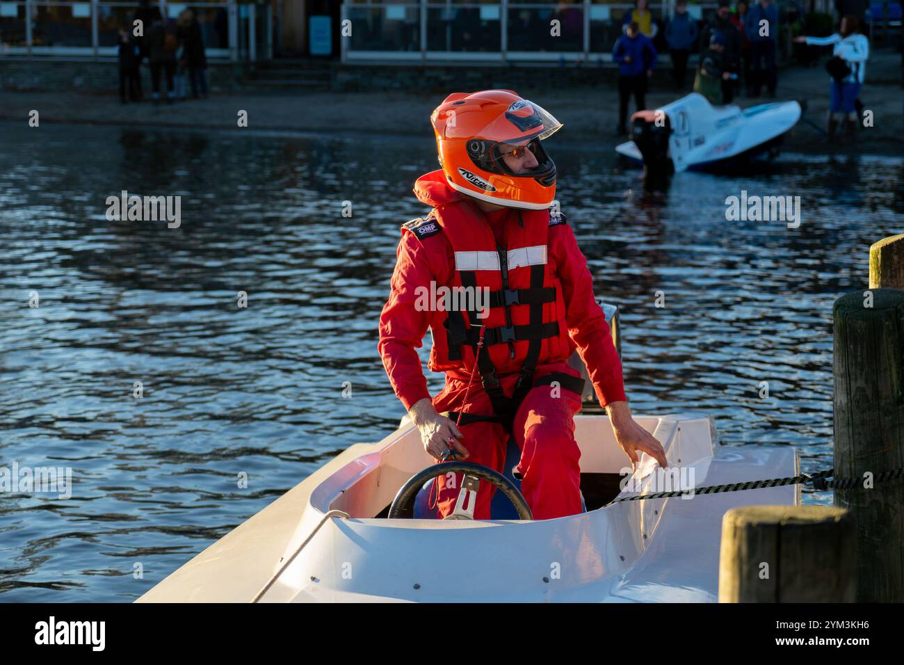 Autista di motoscafo che indossa tute arancioni luminose in piedi sulla sua barca in attesa di scendere a terra alla Coniston Power Boat Records Week. Foto Stock